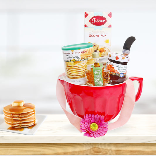Red mixing bowl with pancake mix, syrup, and other items on a white background