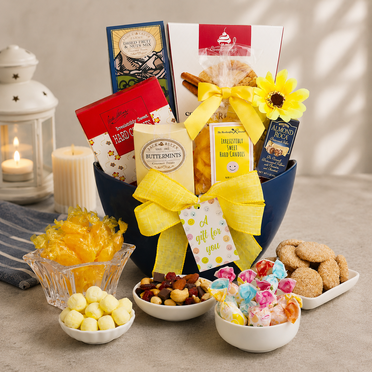 Gourmet gift basket with candies, cookies, and a candle on a wooden surface.