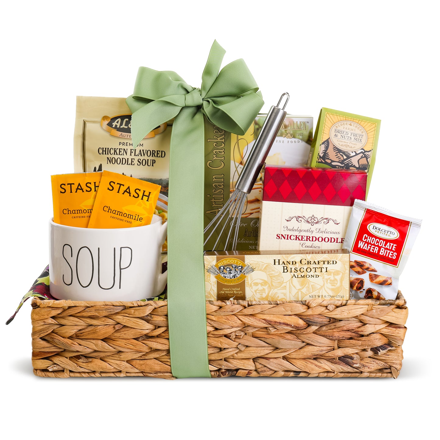 A woven straw gift basket filled with assorted snack and food items, tied with a large sage green ribbon. Visible contents include a white ceramic mug labeled 'SOUP' with Stash chamomile tea packets, chicken flavored noodle soup, a box of Snickers Snickerdoodle cookies, a bag of handcrafted biscotti, chocolate water bites, and a whisk.