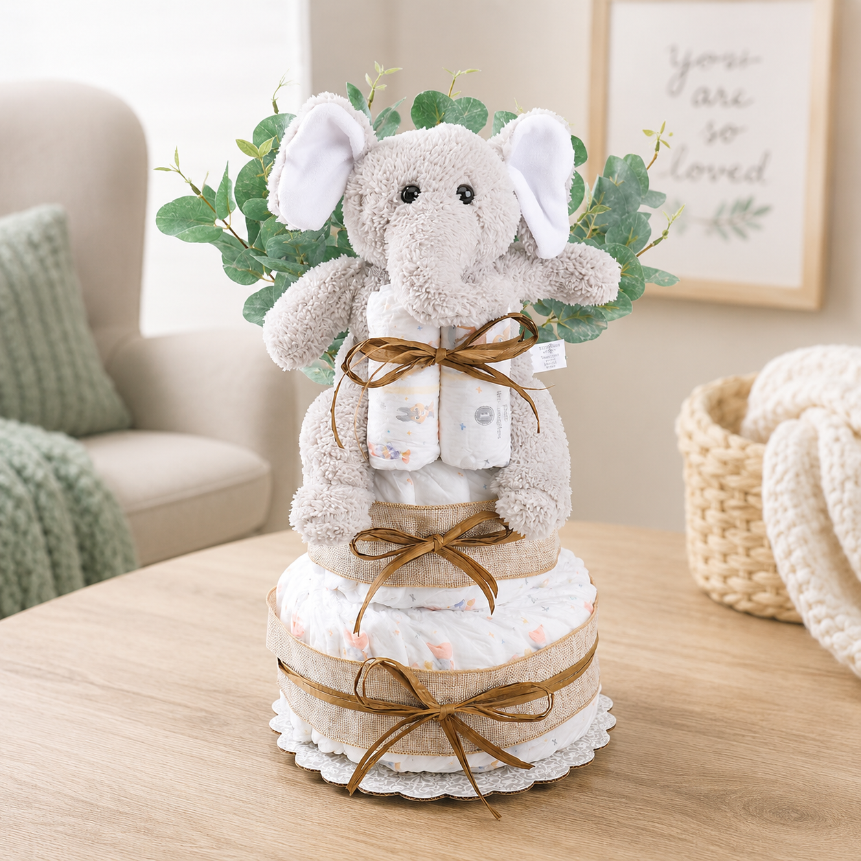 Decorative diaper cake with plush elephant toy on a wooden table.