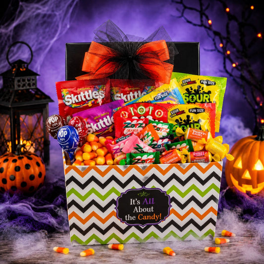 A Halloween-themed candy gift basket filled with assorted candy, decorated with a black and orange bow and a chevron-patterned box. The scene is set against a spooky purple background with a lit jack-o'-lantern, a lantern, and cobwebs.