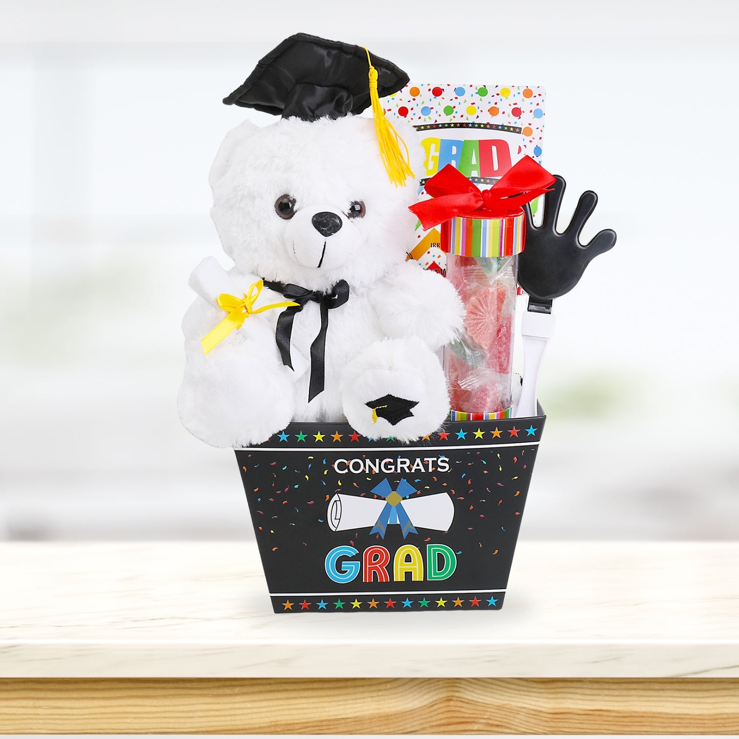 Graduation-themed gift basket with teddy bear, candy, and cap on a white background